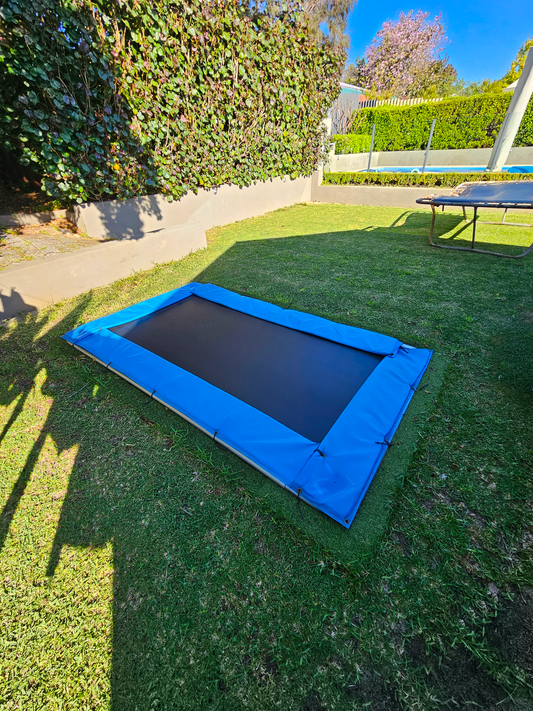 Rectangular inground trampoline in garden with above ground trampoline and pool in background