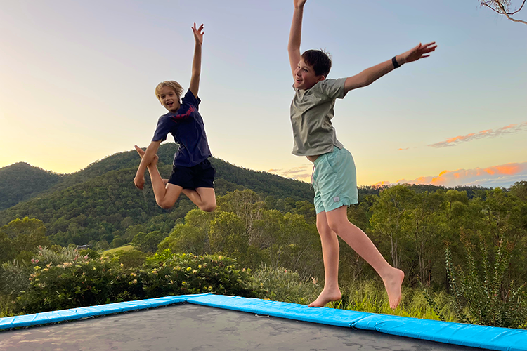 Two children jumping on a trampoline with a scenic mountain background