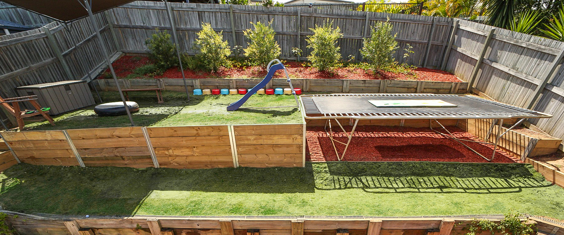 Backyard with trampoline, slide, and sand pit.